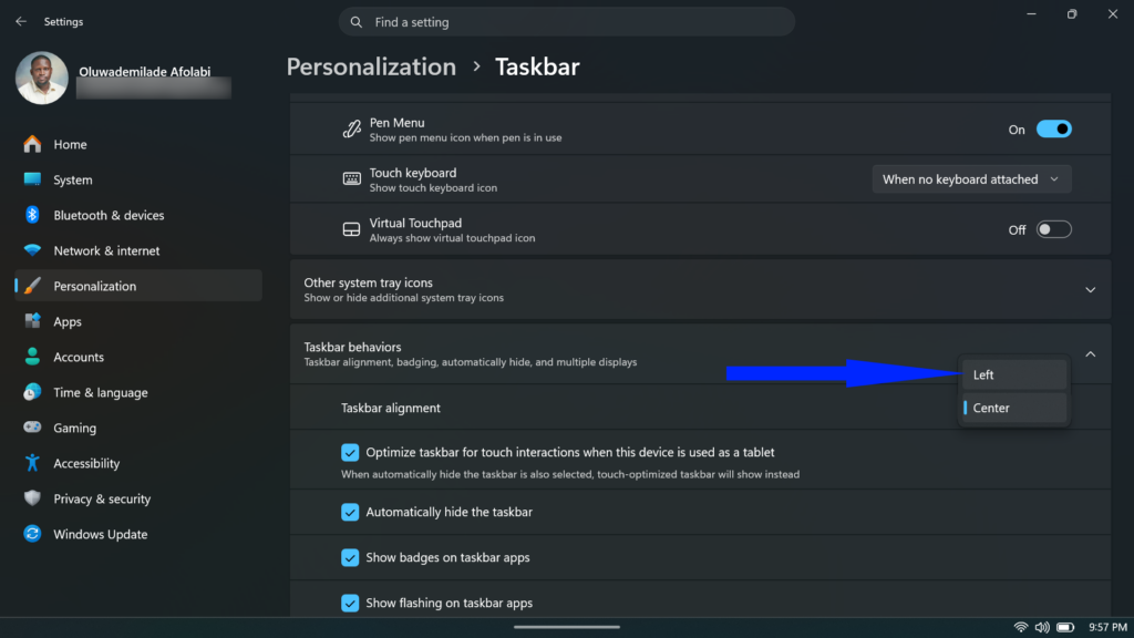 Windows 11 Taskbar settings page with a blue arrow pointing to the Left alignment option within the Taskbar behaviors section.